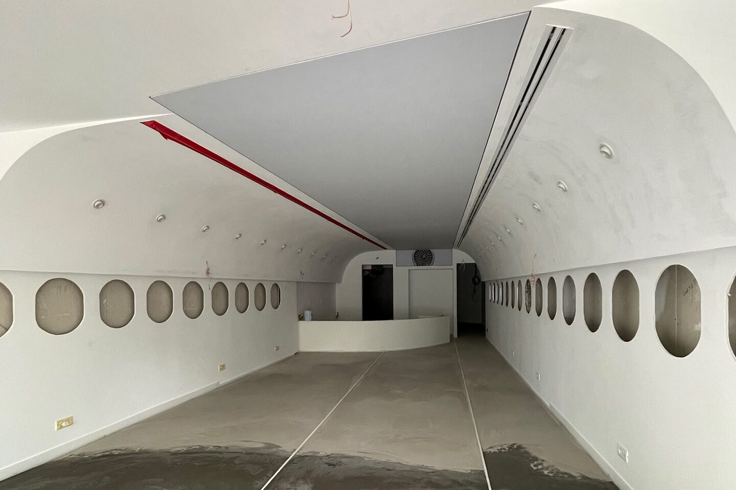 The plastered shell with the fuselage arch formed in the ceiling, window openings in both walls and a bare concrete floor.