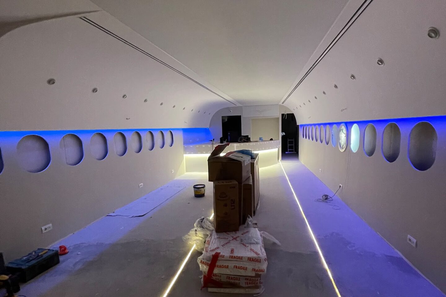 Lighting test during the build: blue cove light along the ceiling edge and the floor light lines lit, pallets still on the floor.
