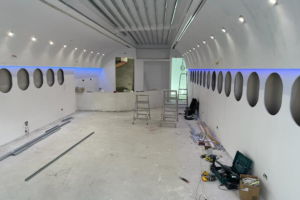 The bare concrete shell during construction: oval window openings cut through the sidewall, a ladder and tools on the floor.