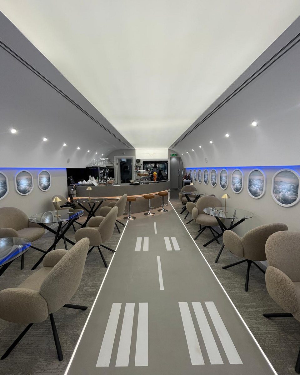 As built: the finished café down its centreline, runway markings on the floor and backlit oval windows along both walls.
