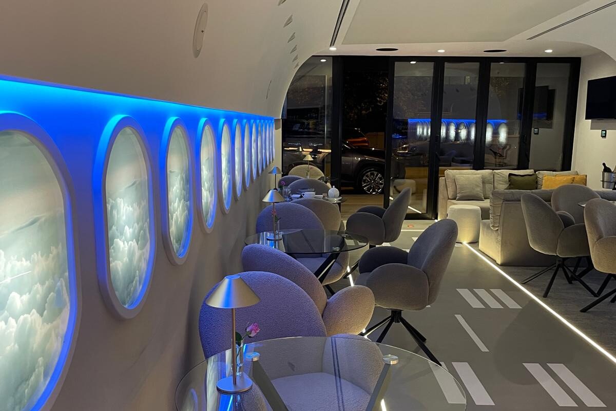 The finished lounge at night: backlit cloud windows and a blue cove along the wall over glass tables and boucle chairs.