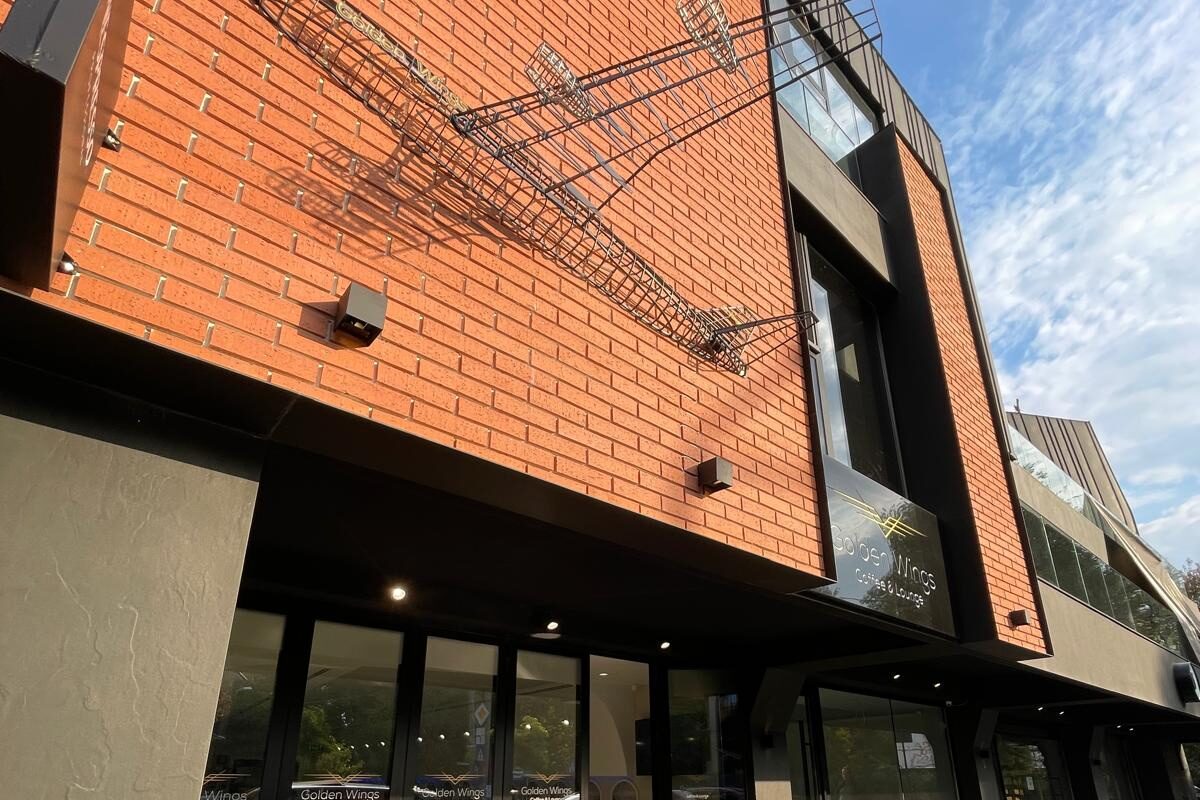 Street elevation with the outdoor terrace in use and a wire aeroplane sculpture on the brickwork.