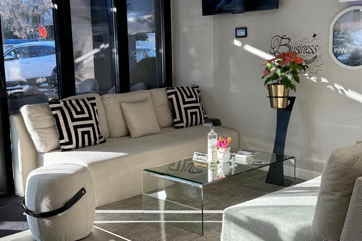 The lounge end of the room: pale sofas around a glass table, a screen on the wall and the street through full-height glazing.