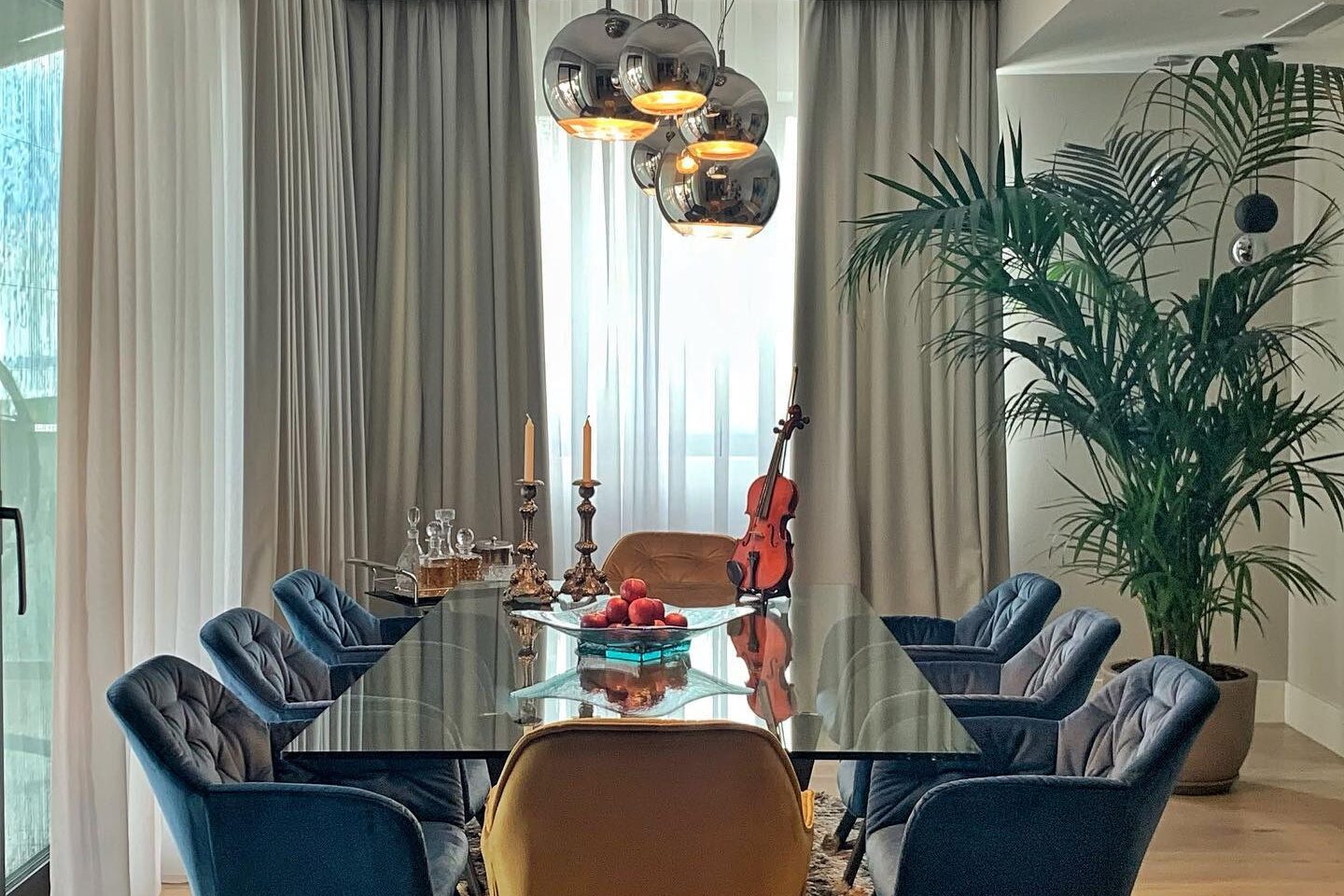 Dining room: glass-topped table with blue velvet chairs and one tan leather head chair, copper globe pendants above.