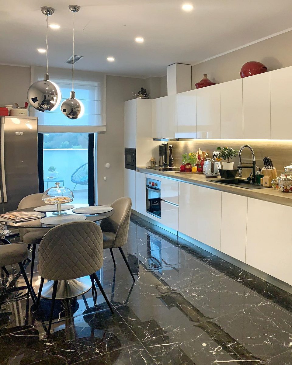The kitchen run in gloss white over a black marble floor, with a round dining table in the foreground.
