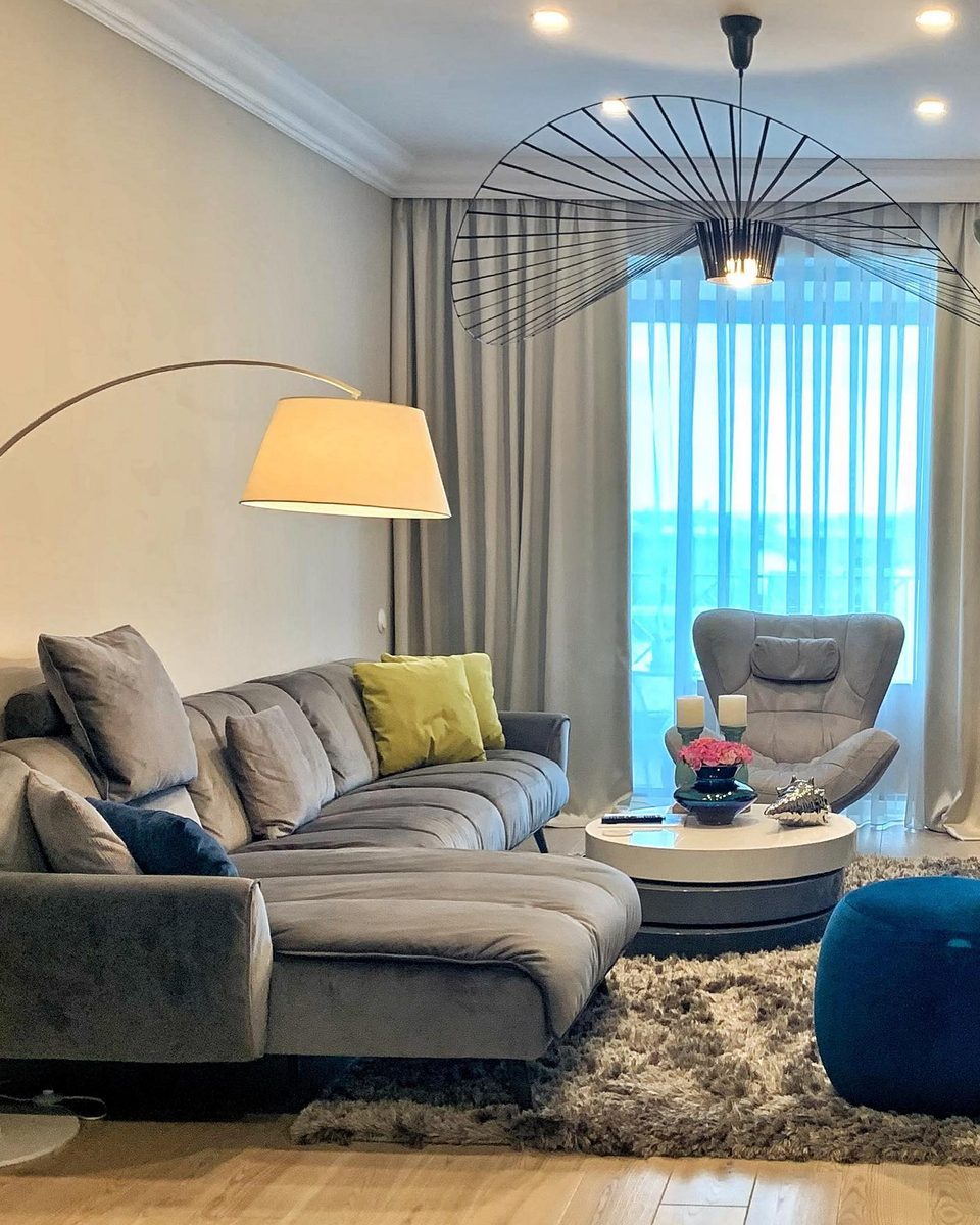 Living room: L-shaped grey sofa with mustard and navy cushions under an arc floor lamp.