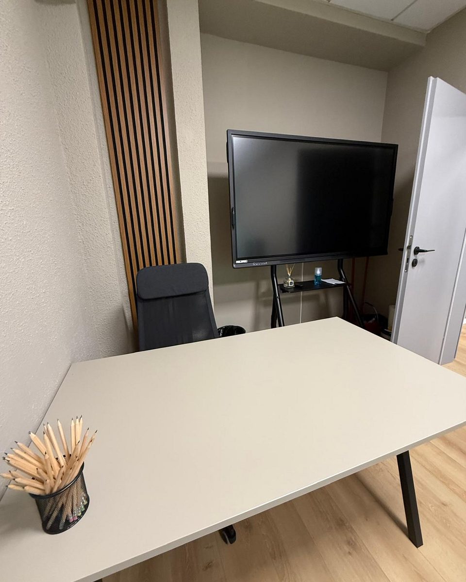 Breakout corner: a white meeting table under a wall-mounted screen beside the slatted panelling.