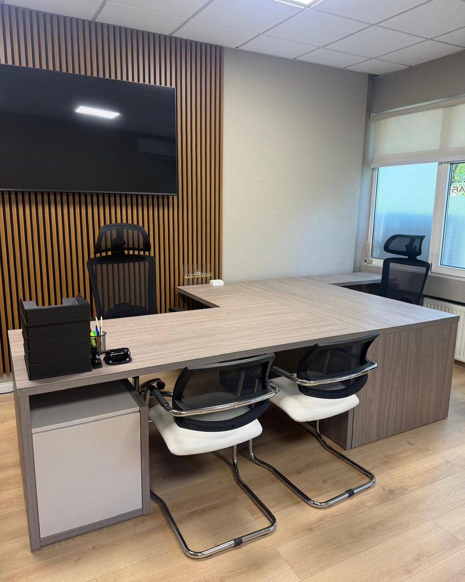 Director office: L-shaped oak-veneer desk with white cantilever visitor chairs against a slatted acoustic wall.