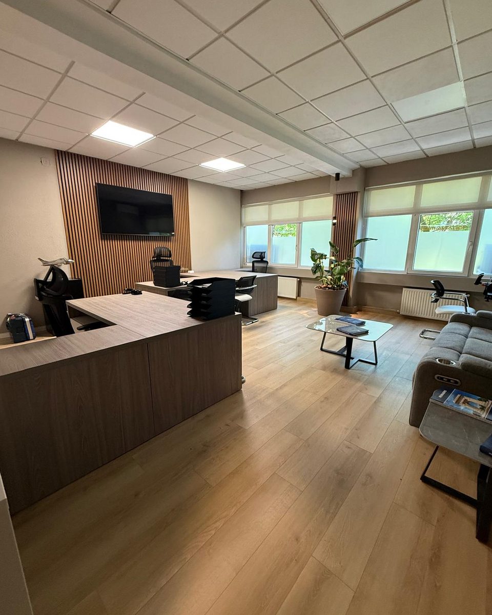 The open-plan room from the reception counter: oak floor, sofa, planting and the slatted screen wall.